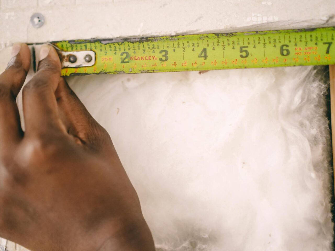 Close-up of a hand measuring insulation with a yellow tape measure.