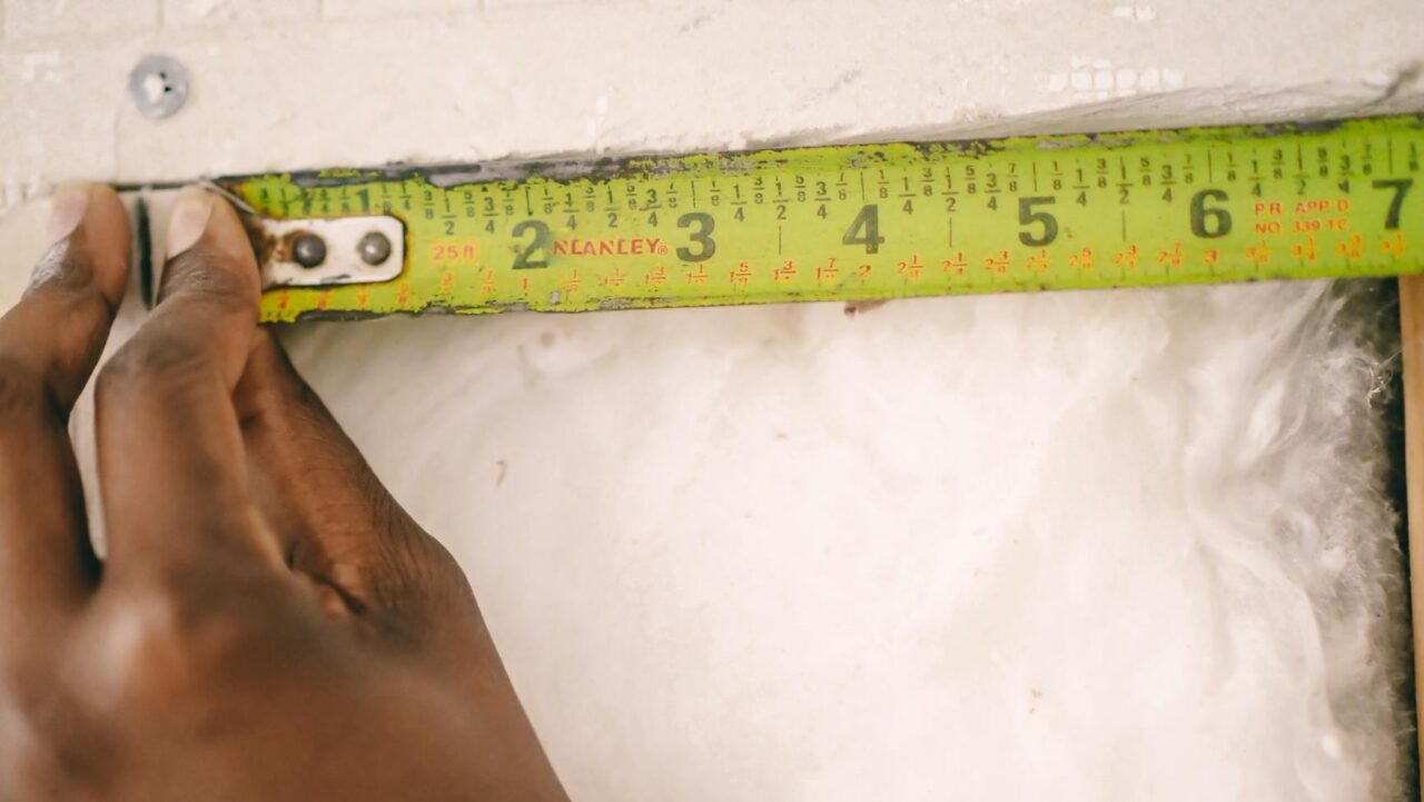 A hand measuring insulation with a yellow tape measure.