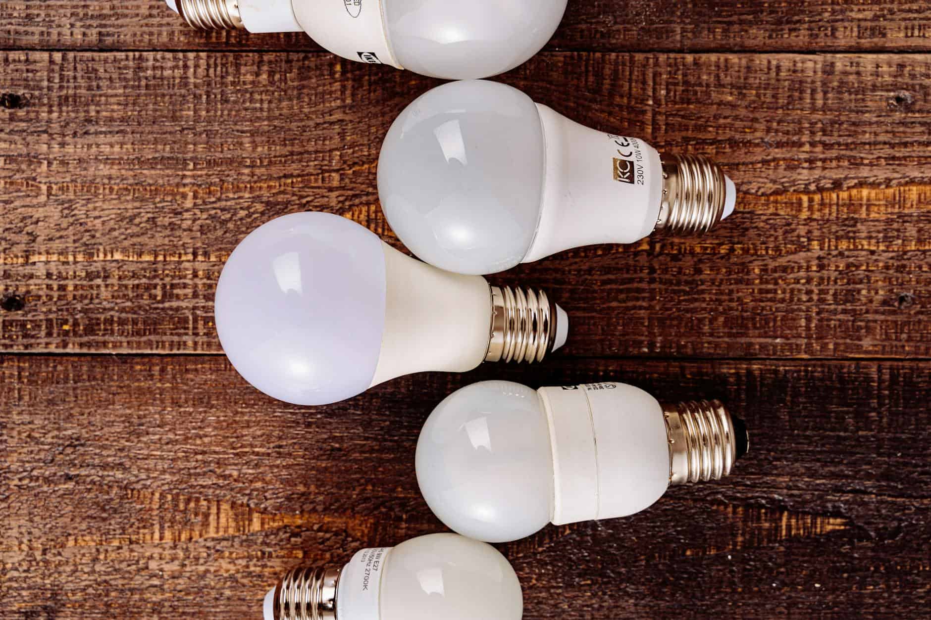 Five white LED light bulbs with different shapes and designs arranged in a row on wooden surface