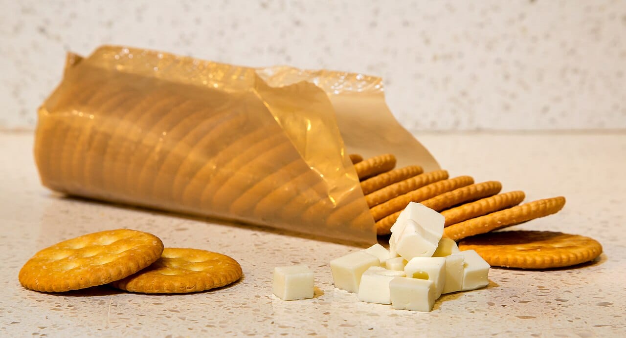 Crackers stacked next to an open package, small cubes of cheese in front, snacks ready to be eaten, savory snack combination, crackers and cheese pairing