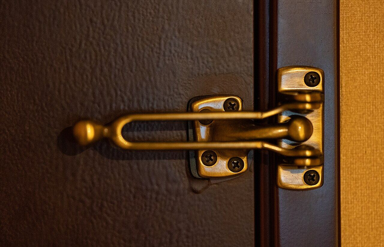 Close-up of a metal door lock with a latch mechanism, showing the lock's brass finish and mounting screws, securely fastening the door, used for added security, the latch is in a locked position on a dark door surface