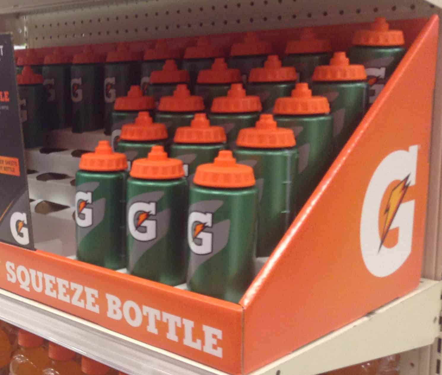 Gatorade squeeze bottles on display, green bottles with orange caps, neatly arranged on a shelf, labeled "SQUEEZE BOTTLE," brightly colored promotional packaging, store aisle, visible
