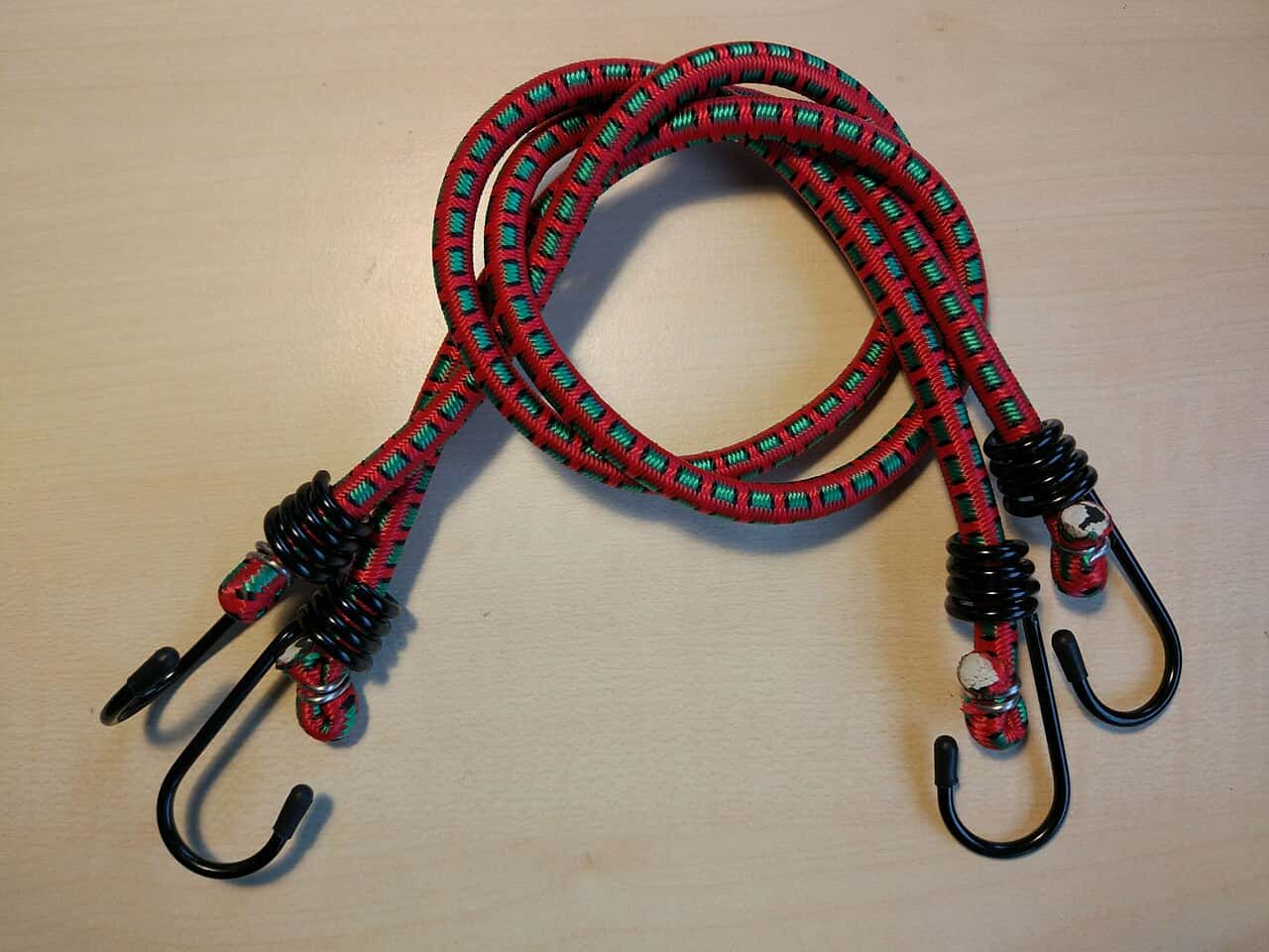 Bungee cords with black metal hooks, colorful red and green patterned elastic material, coiled metal ends, sturdy hooks for securing items, flexible and adjustable tension, used for fastening luggage, securing cargo
