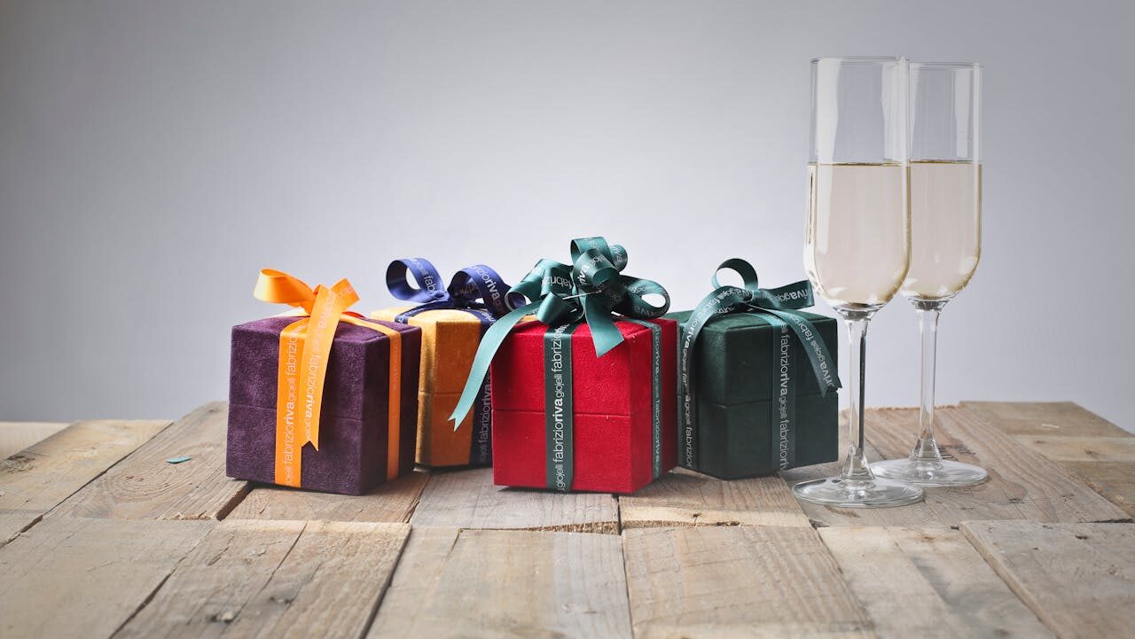 Colorful gift boxes with decorative ribbons, placed on a rustic wooden table, two champagne glasses filled with sparkling wine, festive celebration setup, elegant and joyful atmosphere