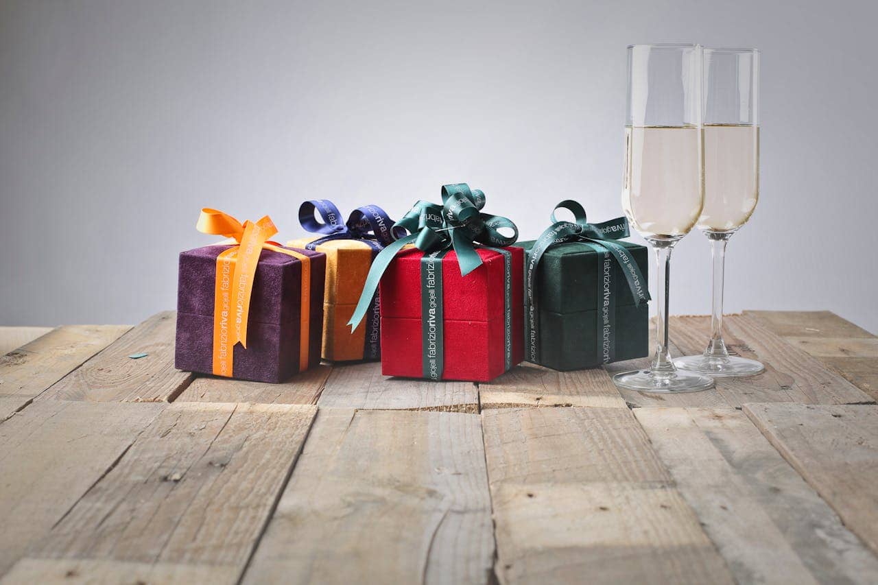 Colorful gift boxes with decorative ribbons, placed on a rustic wooden table, two champagne glasses filled with sparkling wine, festive celebration setup, elegant and joyful atmosphere