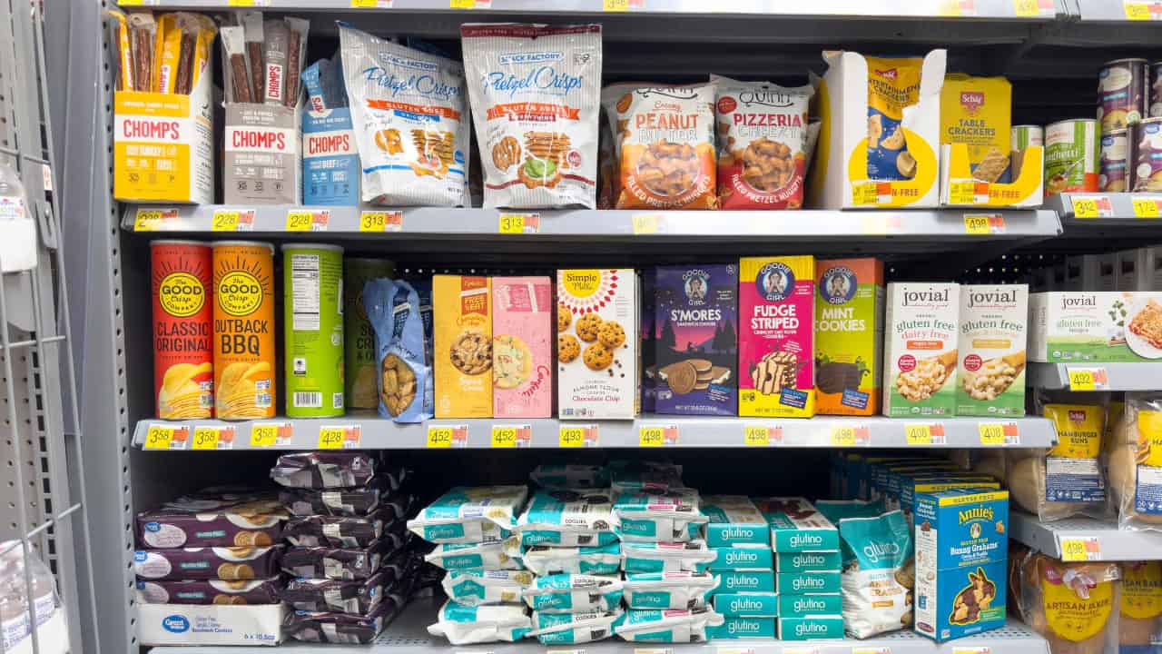 Assorted packaged snacks on store shelves, including cookies, crackers, and chips, colorful packaging, price tags visible