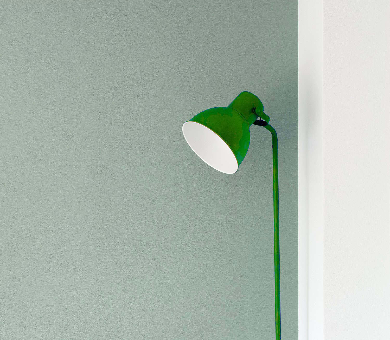 A green floor lamp with a white interior shade, positioned at an angle against a light green wall, modern and minimalistic design, simple and clean aesthetic, lamp not turned on