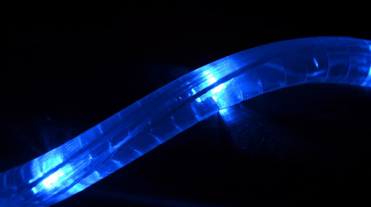 A close-up of a blue LED light strip glowing in the dark, showcasing the flexible, illuminated tubing, light reflecting off the surface beneath, creating a bright, vibrant blue glow