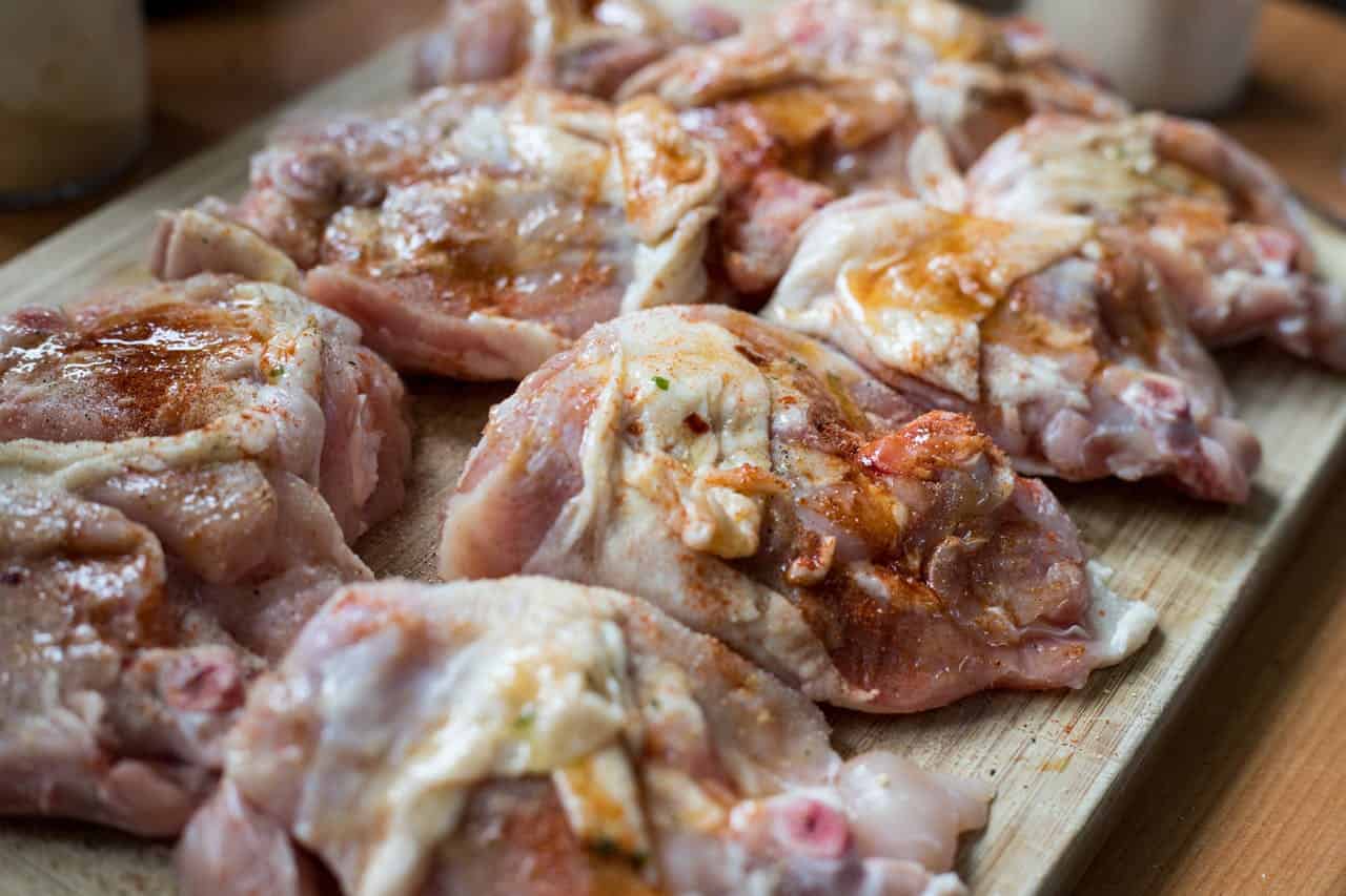 Raw chicken thighs seasoned with spices, arranged on wooden cutting board, preparing for cooking, close-up of marinated meat