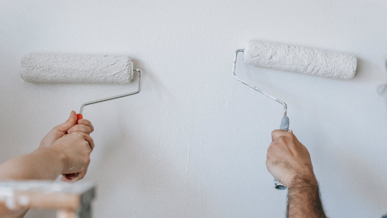 Two people painting a white wall, using paint rollers, working together, home renovation, DIY project
