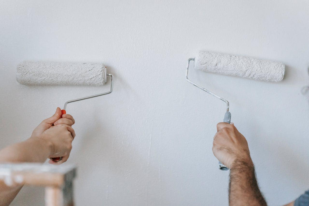 Two people painting a white wall, using paint rollers, working together, home renovation, DIY project