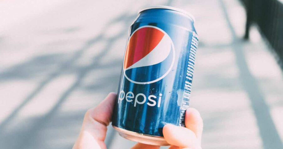 Hand holding a blue Pepsi can, condensation on the surface, blurred outdoor background, bright lighting, carbonated soft drink