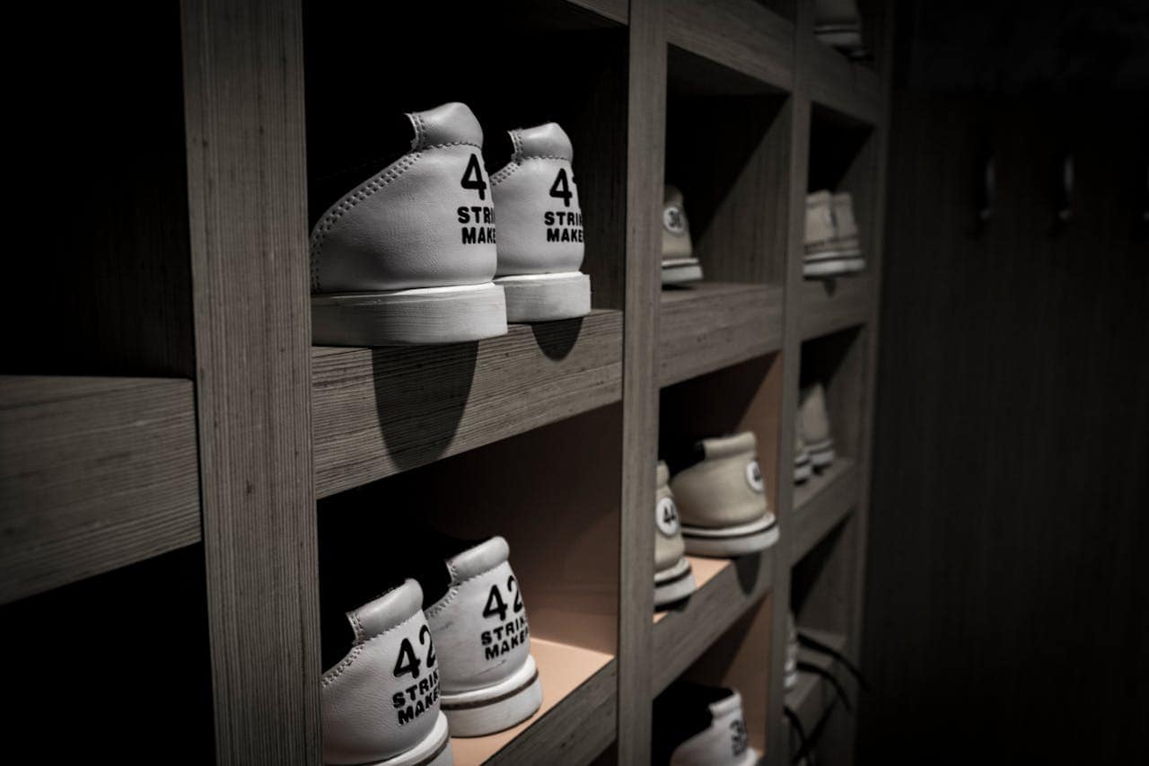 Neatly arranged shoes on wooden shelves, dim lighting, white sneakers with "42" printed on the back, organized storage, minimalist design, modern shoe rack, stylish and functional closet space