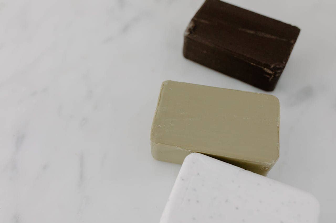 Dark brown, beige, and white soap bars arranged on white surface, blue checkmark icon in upper corner, antibacterial soap samples