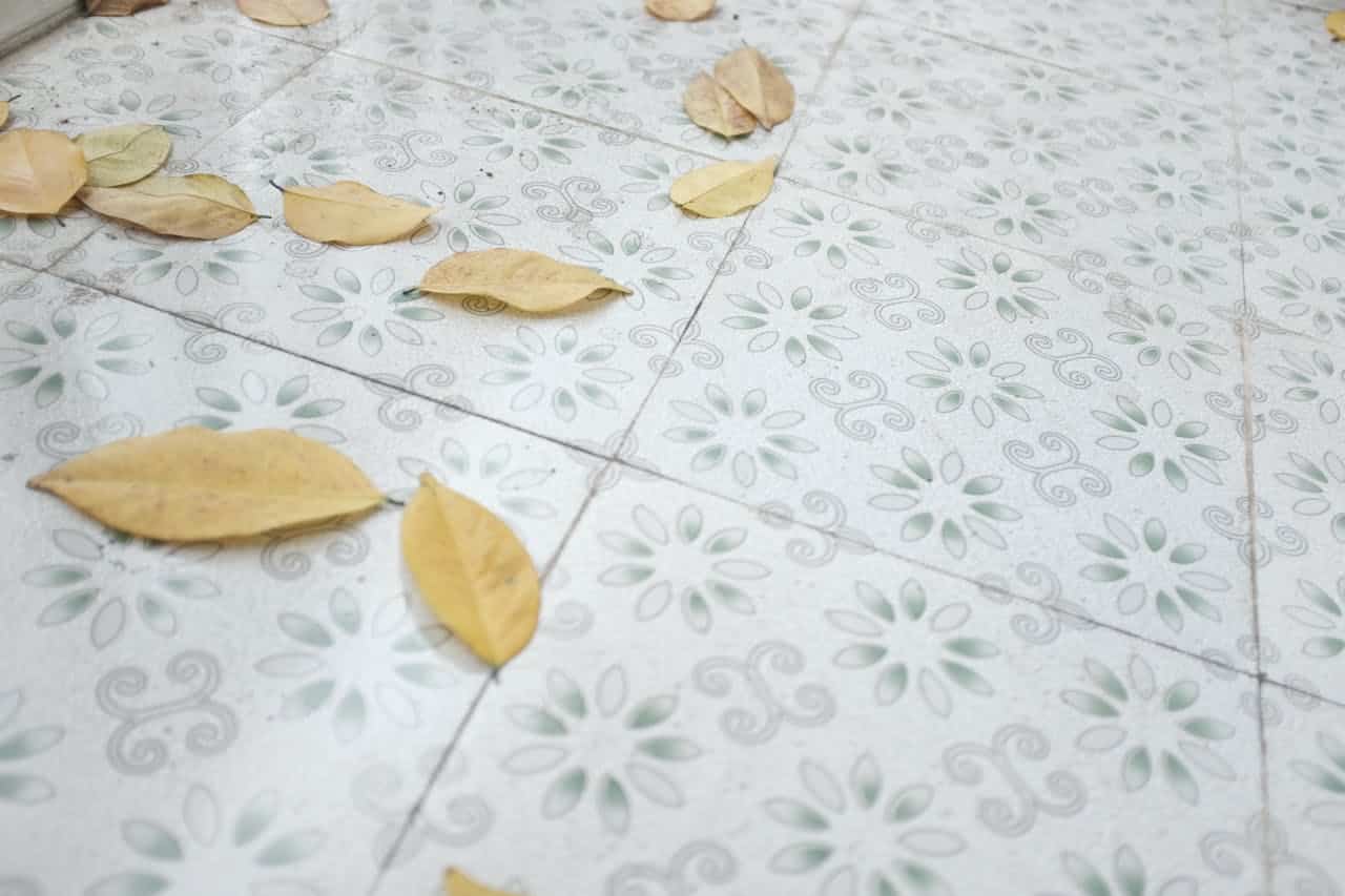 Yellow leaves scattered on patterned floor tiles, floral tile design, signs of dust and wear, outdoor or balcony setting