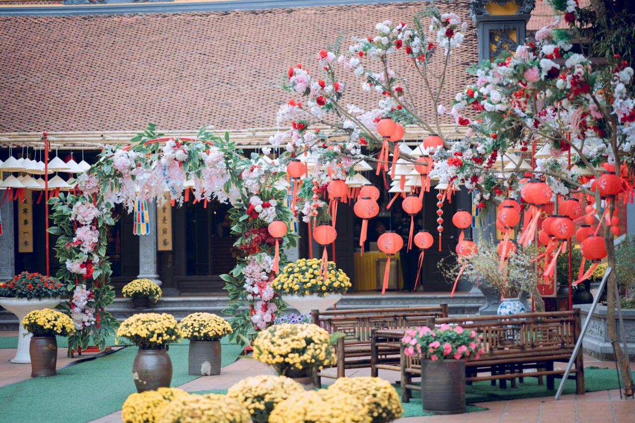 Traditional courtyard decorated with red lanterns, blooming trees, yellow chrysanthemums, and wooden benches for festive celebration