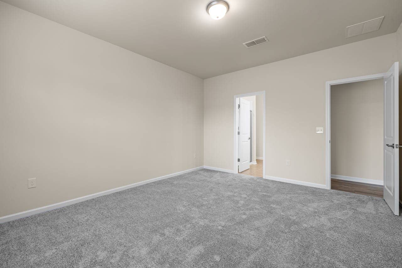 Empty room, beige walls, gray carpet, white doors, bright ceiling light, open doorways, neutral color scheme