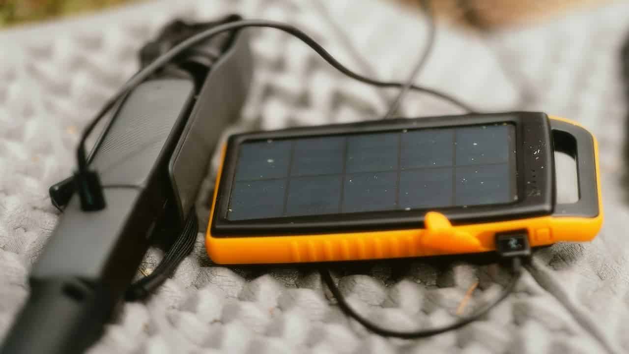 Orange and black portable solar charger with connecting cable next to black power bank on textured light surface