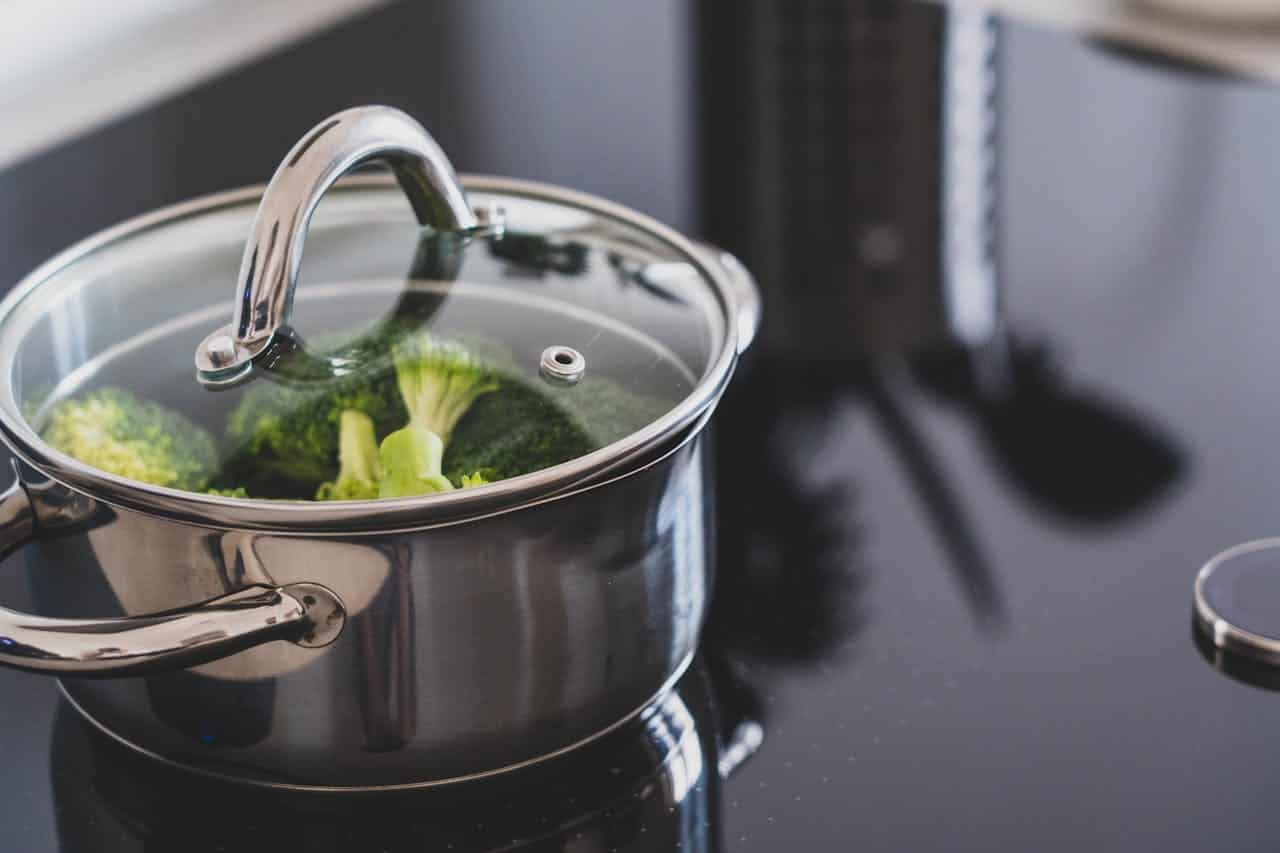 Stainless steel pot with a glass lid, steaming broccoli on a black induction stove, healthy cooking, blanching vegetables, modern kitchen setting