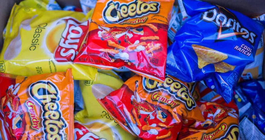 A close-up of several bags of snacks, including Cheetos, Fritos, and other chip varieties, with bright packaging in yellow, orange, and blue, stacked together
