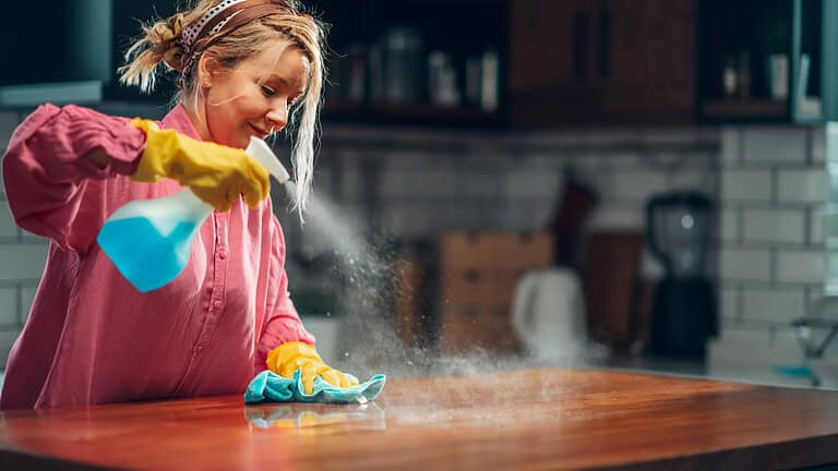 Young woman wearing yellow gloves, spraying an oil-based wood cleaner on a wooden surface, wiping with a cloth, creating a mist effect, cleaning a kitchen countertop, focused expression, cozy home setting