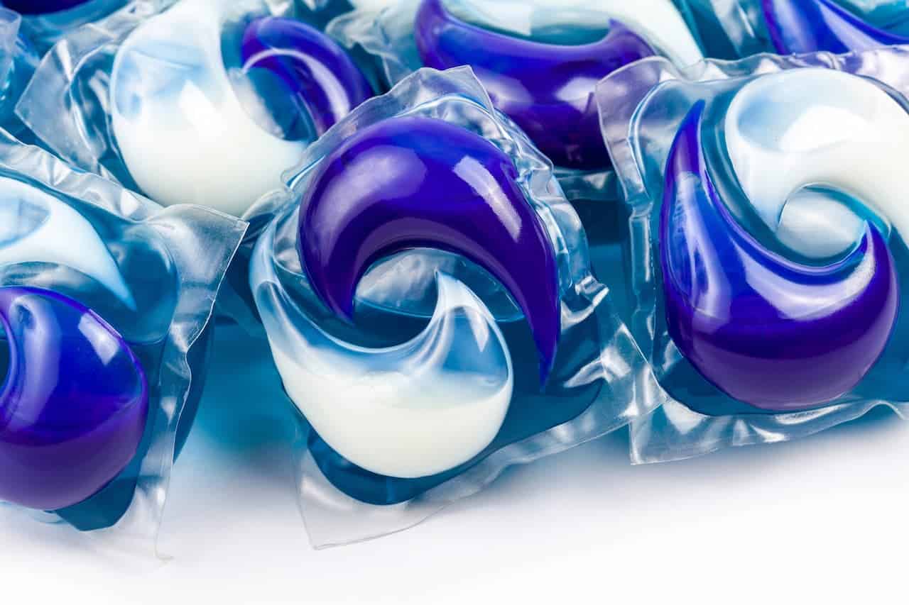 Close-up of laundry detergent pods, glossy blue and white liquid-filled capsules, individually wrapped in dissolvable plastic, piled together, used for washing clothes
