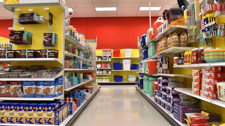 Aisle in a retail store, colorful shelves filled with household products, bright red and yellow walls, containers and cleaning supplies on display, organized rows, store layout with various plastic items, aisle well-lit, clean floor, shopping environment