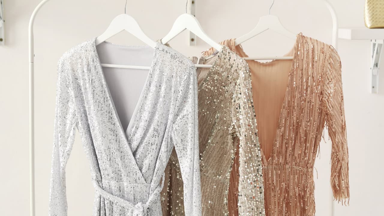 Several women's garments hanging on a clothing rack, including a white wrap-style top or dress and beige or tan colored clothing items with textured or lace details