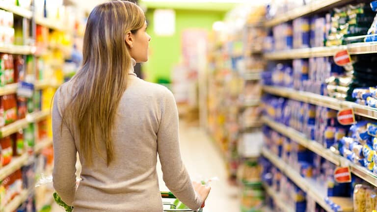 Woman shopping in a grocery store, pushing a cart, looking at products on store shelves, colorful aisle, supermarket environment, focused on choosing items, store labels visible, browsing for items