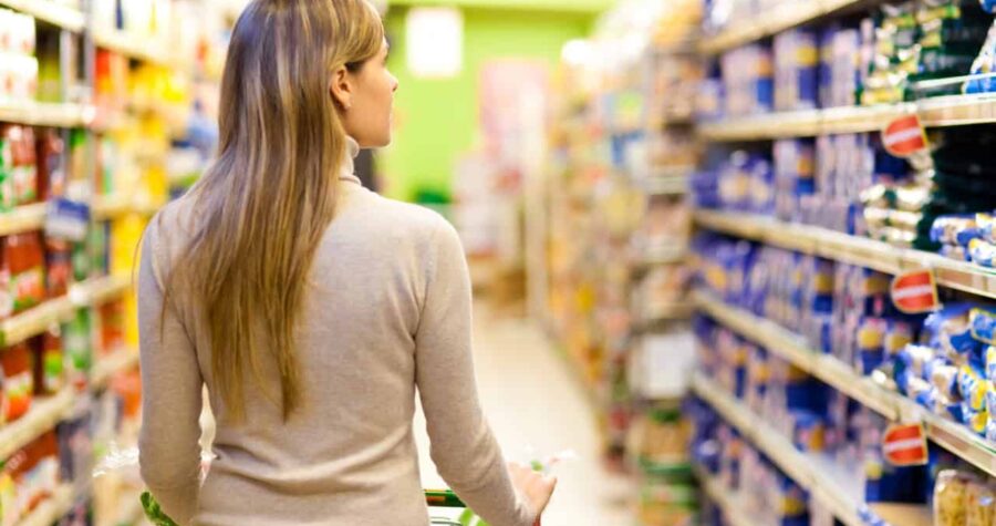 Woman shopping in a grocery store, pushing a cart, looking at products on store shelves, colorful aisle, supermarket environment, focused on choosing items, store labels visible, browsing for items