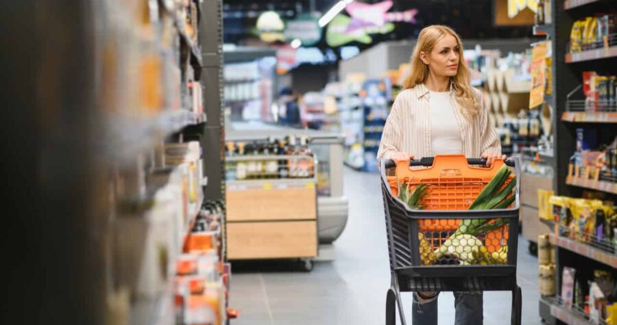 Woman shopping in a supermarket, pushing a cart filled with groceries, looking at products on the shelves, grocery store aisle, focused on shopping