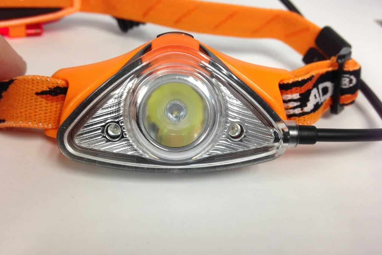 Triangular LED headlamp with bright central bulb mounted on orange adjustable headband with black and orange elastic straps