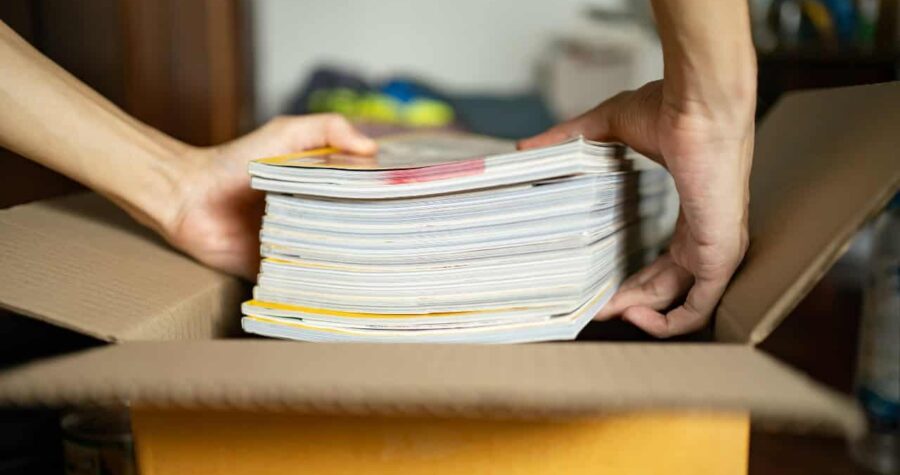 A person holding a stack of magazines, organizing magazines in a box, sorting through a pile of magazines, preparing magazines for storage, handling a stack of old magazines