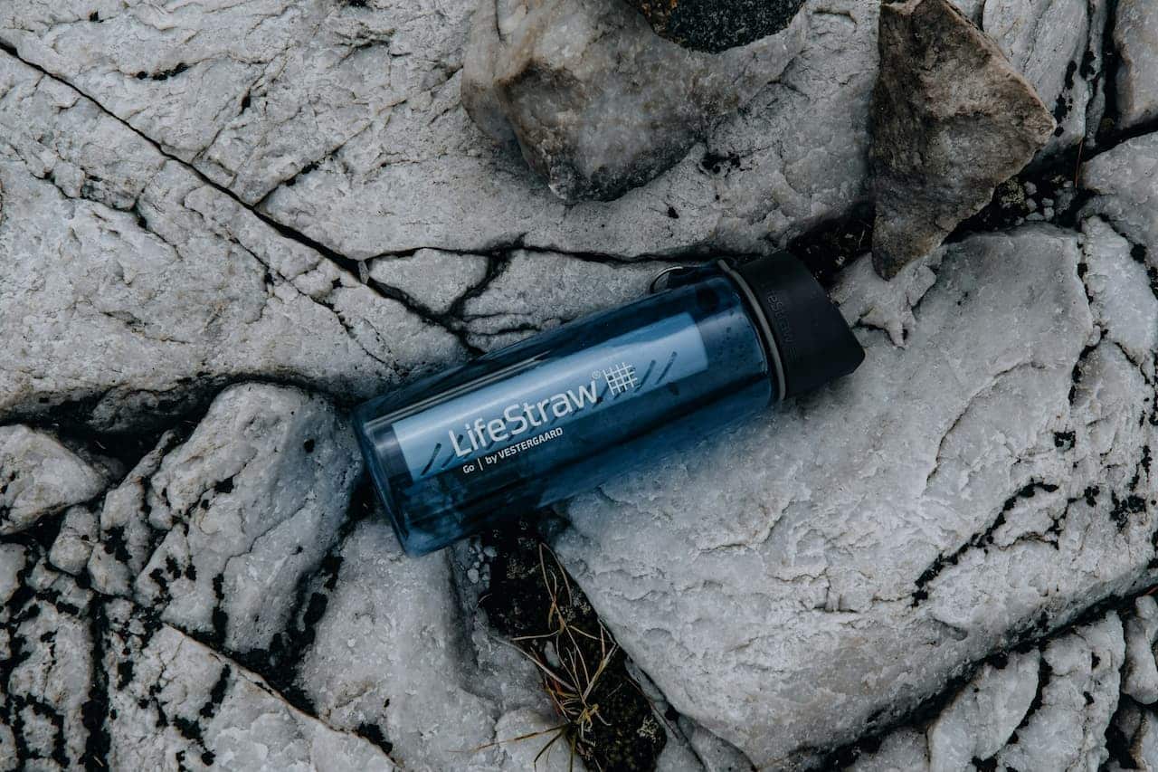 Blue LifeStraw Go water filtration bottle lying on cracked white limestone rock surface outdoors with black cap visible