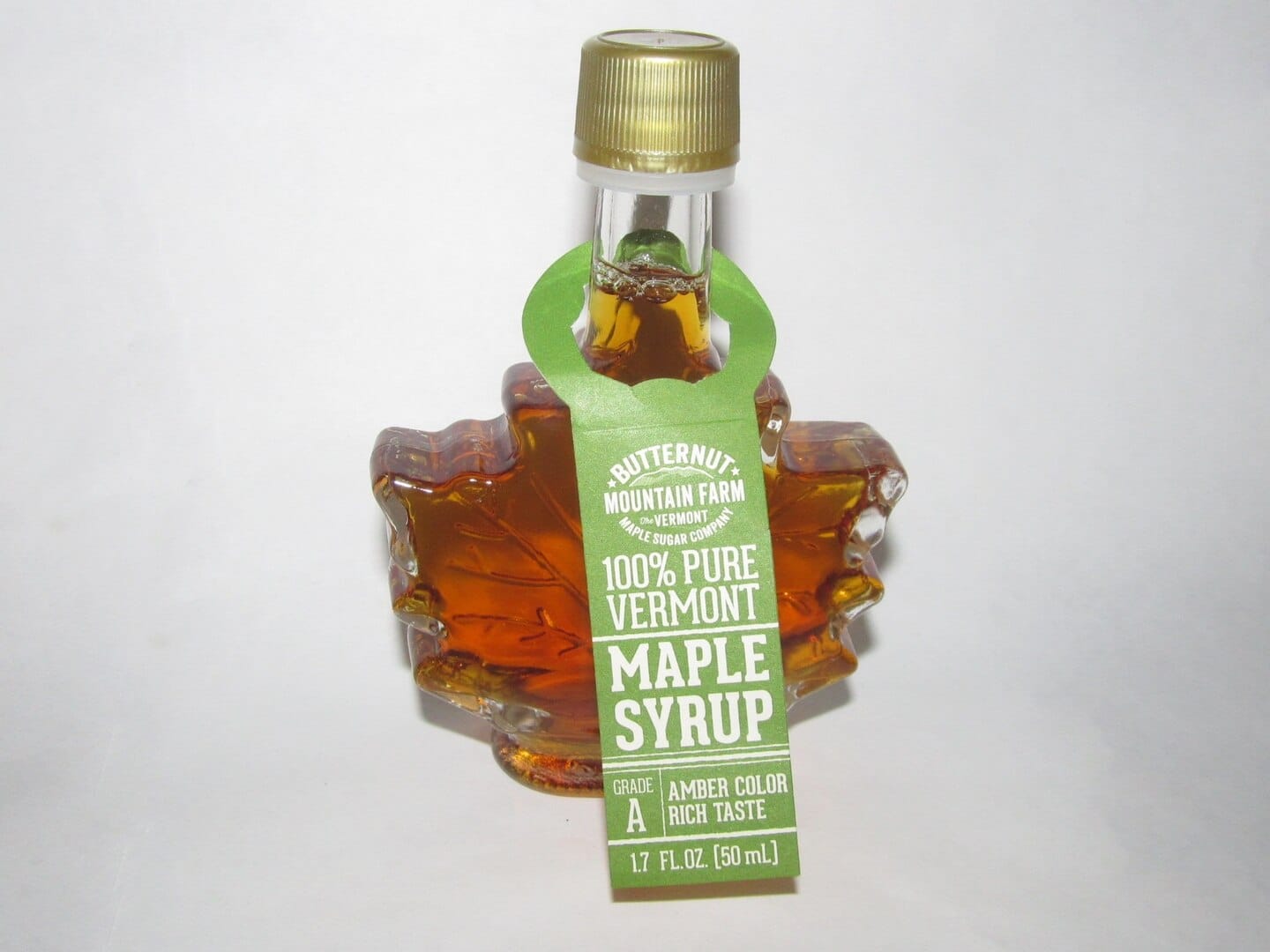 Maple leaf-shaped glass bottle of Butternut Mountain Farm 100% Pure Vermont Maple Syrup, amber color, Grade A, 1.7 fl. oz, green label, gold cap, white background