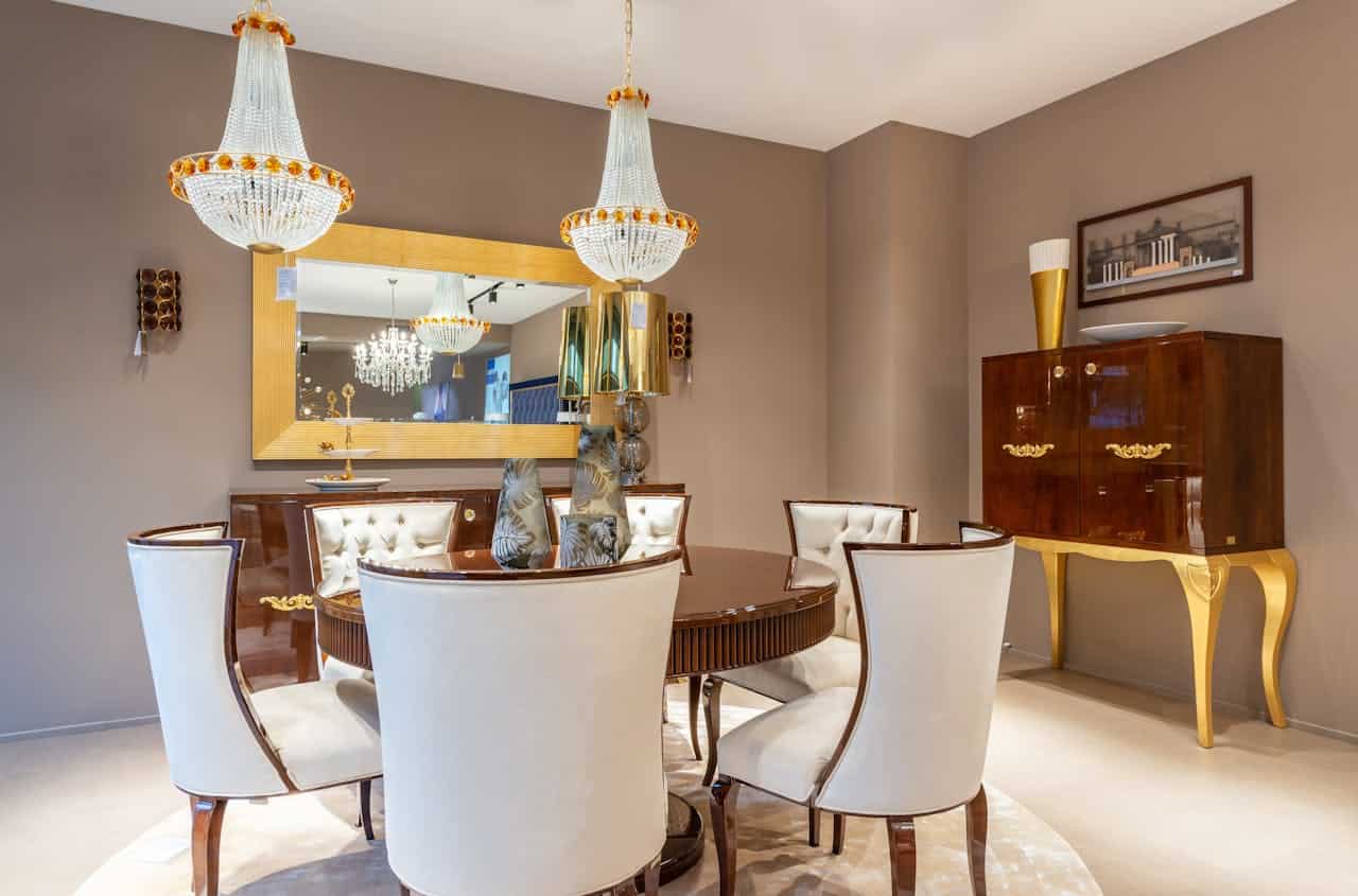 Elegant dining room, bold crystal chandeliers, warm lighting, luxurious cream and wood furniture, large mirror reflecting chandelier, decorative gold-accented cabinet, modern yet classic interior design