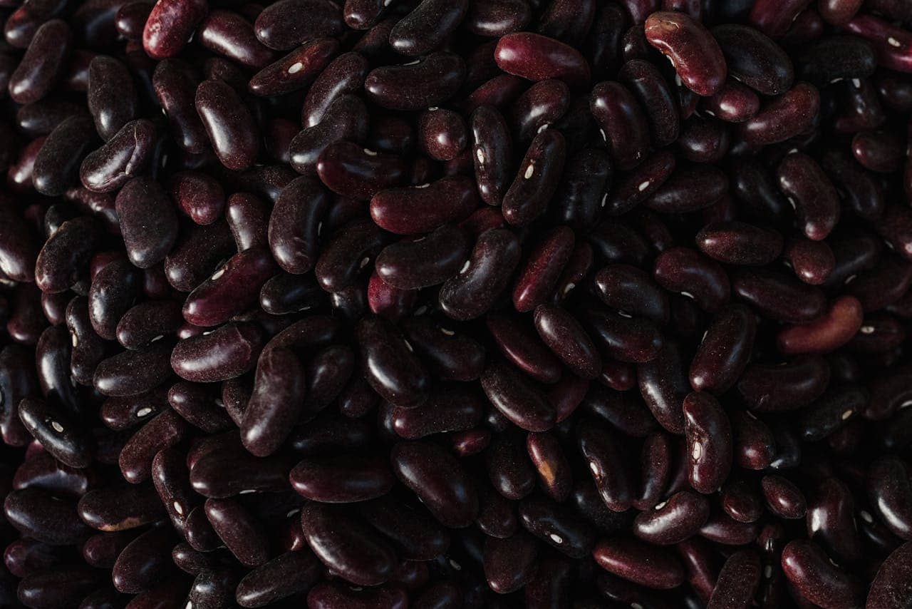 A pile of dark red kidney beans, smooth and shiny, densely packed together, uncooked and ready for cooking, meal preparation, or food storage
