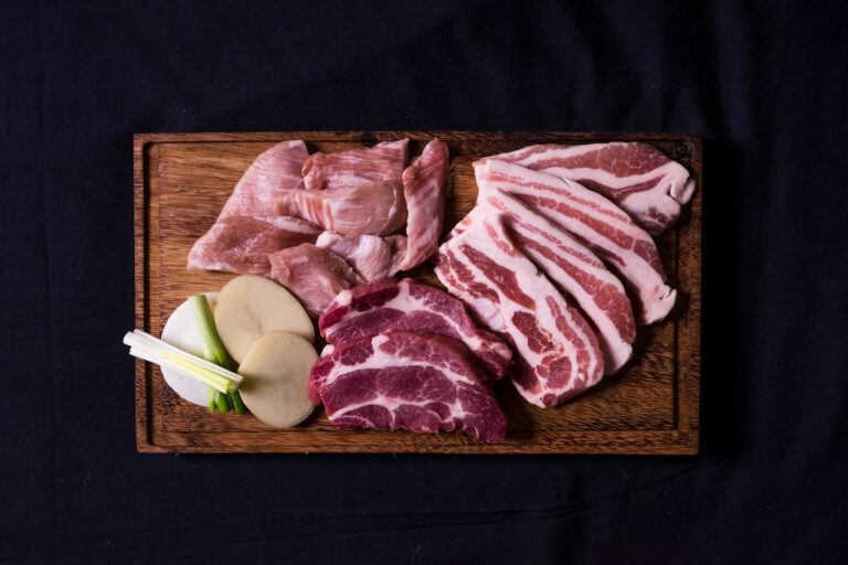 Pork cuts arranged on a wooden cutting board, slices of lean pork, fatty pork belly, green onions, and slices of potatoes