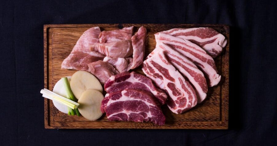 Pork cuts arranged on a wooden cutting board, slices of lean pork, fatty pork belly, green onions, and slices of potatoes