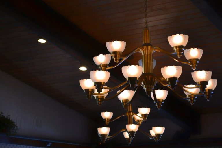 Chandelier with multiple light fixtures, lights glowing softly, decorative flower-shaped bulbs, hanging from the ceiling, wooden ceiling with overhead lighting, warm ambiance, artistic and elegant design, illuminated lights create a cozy atmosphere in the room