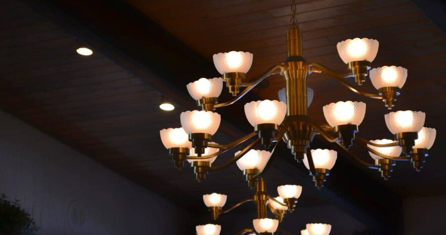 Chandelier with multiple light fixtures, lights glowing softly, decorative flower-shaped bulbs, hanging from the ceiling, wooden ceiling with overhead lighting, warm ambiance, artistic and elegant design, illuminated lights create a cozy atmosphere in the room