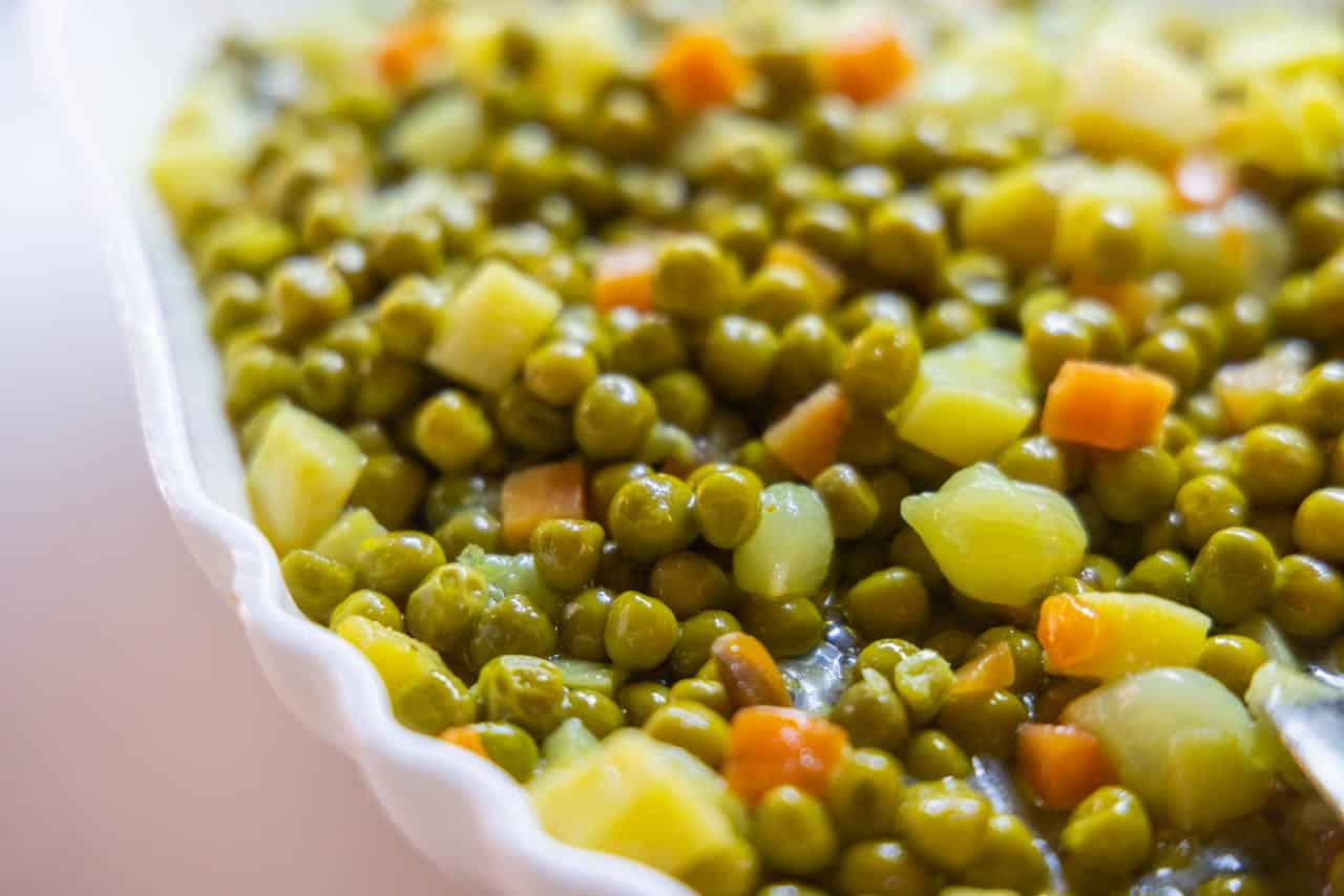 The image shows a close-up of a dish containing green peas mixed with diced carrots and potatoes, the vegetables are arranged together in a white serving dish