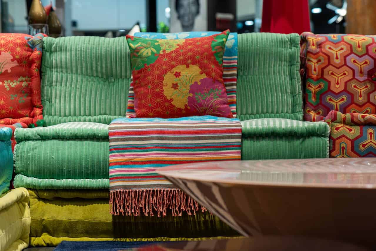 Colorful, cozy seating area with vibrant cushions, green and red fabric chairs, striped blanket, bright patterns, warm tones, decorative accent pillows, modern home interior, eclectic design style