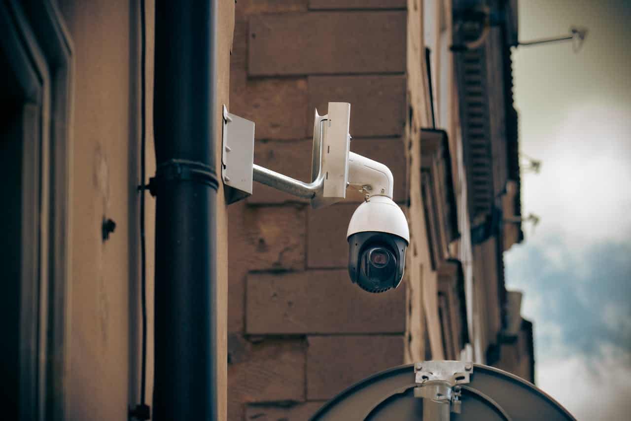 Security camera mounted on a wall, CCTV camera, outdoor surveillance, monitoring system, close-up of a white camera, tracking movement, modern security equipment