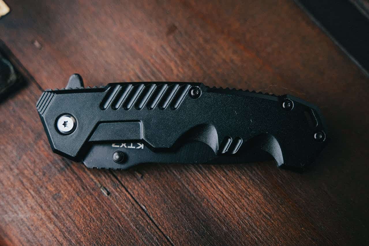 A close-up of a black folding knife, placed on a wooden surface, sharp blade visible, rugged handle design, KTX branding on the handle