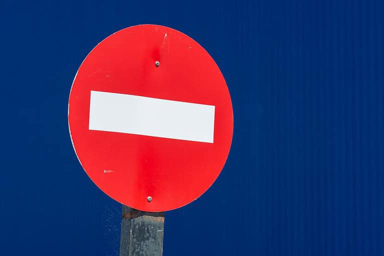Red "Do Not Enter" traffic sign with a white horizontal bar, mounted on a pole, against a blue background
