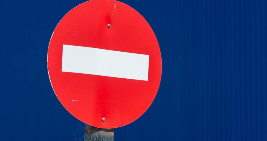 Red "Do Not Enter" traffic sign with a white horizontal bar, mounted on a pole, against a blue background