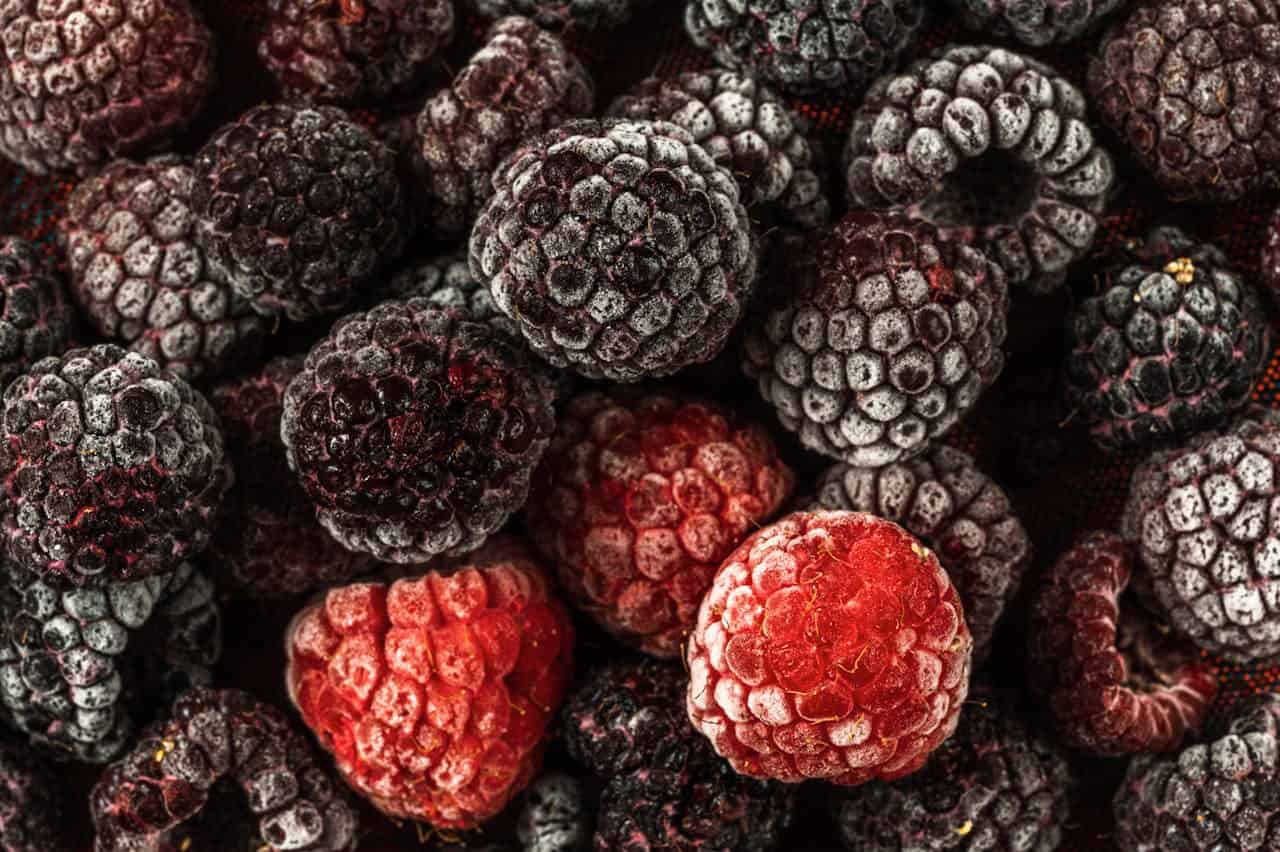 Frozen blackberries and raspberries clustered together, with frost covering most berries except a few bright red ones