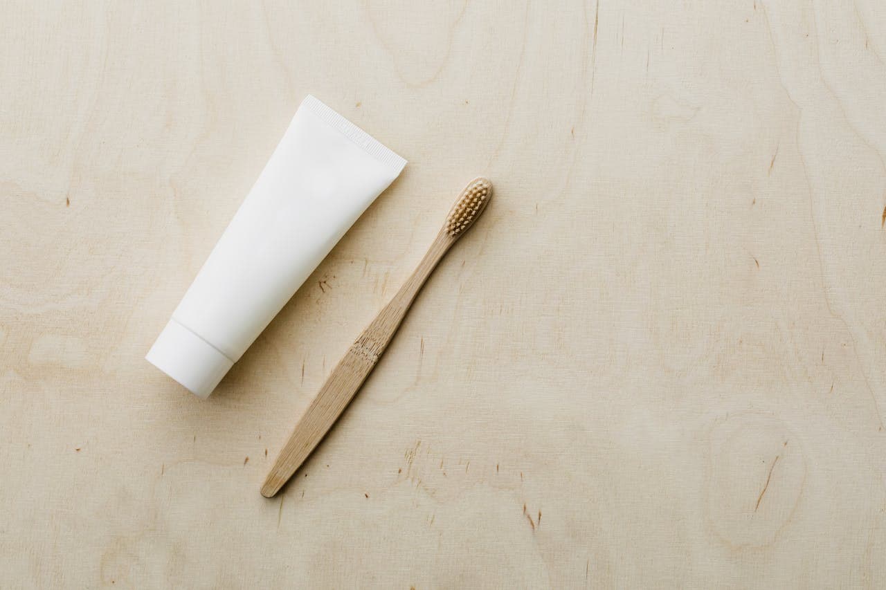 Bamboo toothbrush next to a white tube of toothpaste, placed on a light wooden surface, eco-friendly dental care products