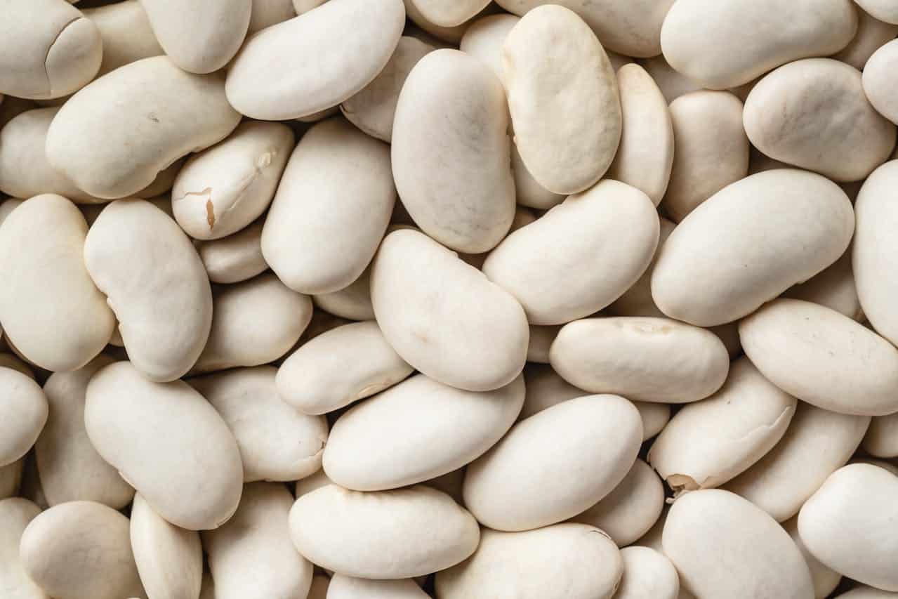 A pile of uncooked white beans, smooth and oval-shaped, densely packed together, ready for cooking, meal preparation, or food storage